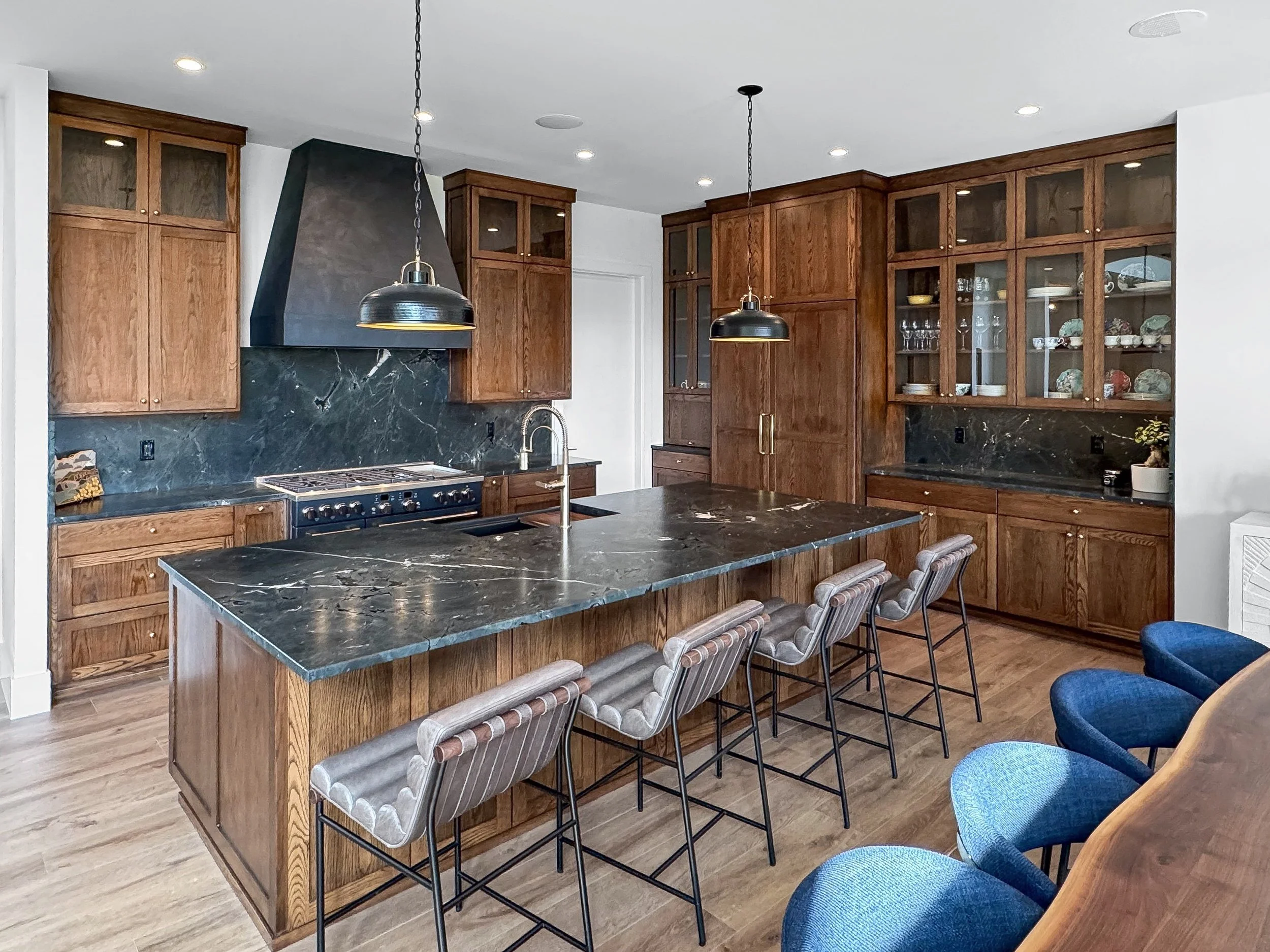 Modern kitchen with wooden cabinets, black marble countertops, and a kitchen island with striped fabric stools.