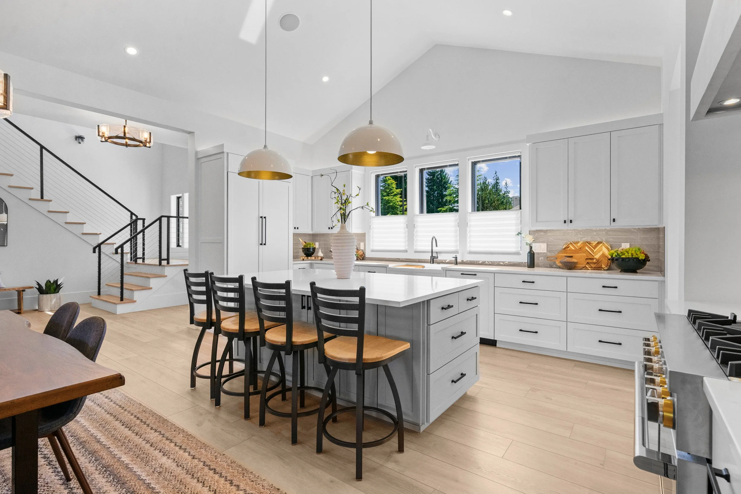Bright, modern kitchen with white cabinets, a large kitchen island, black chairs, pendant lights, and large windows.