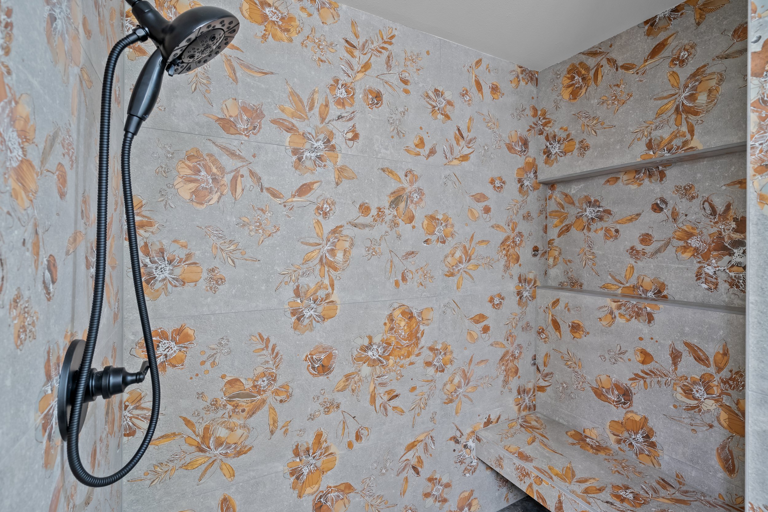 A shower area with floral patterned tiles and a black showerhead attached to a flexible hose.