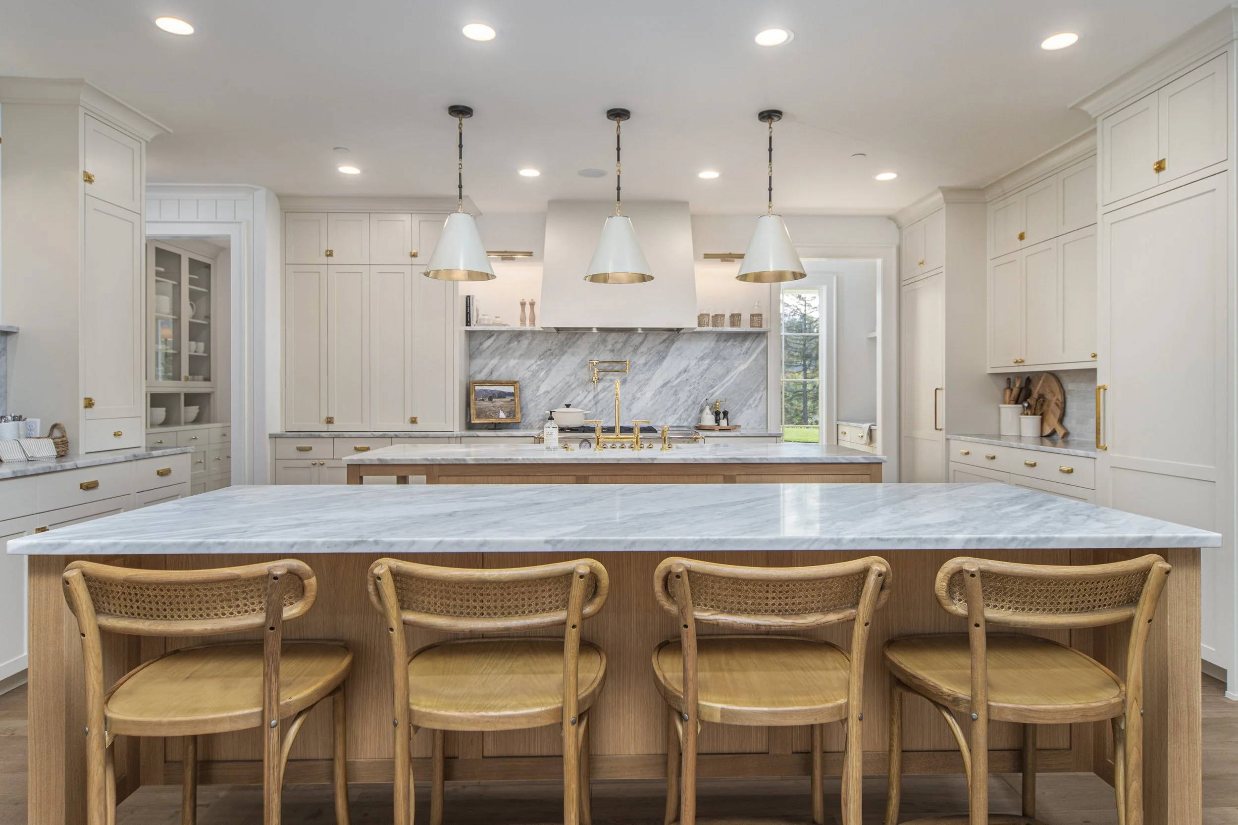 Modern white kitchen with marble countertops, gold fixtures, and a large island with four chairs.