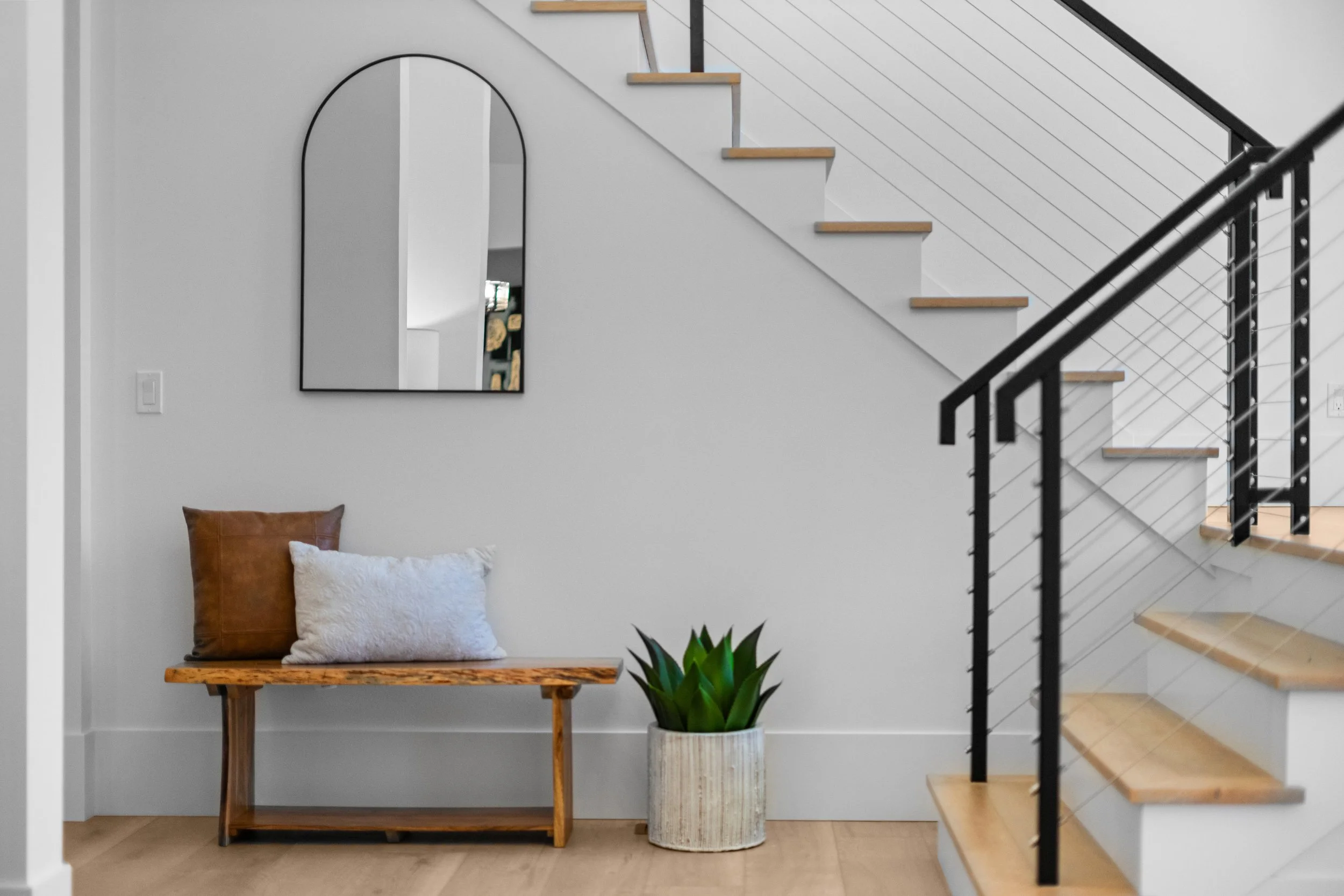 A modern interior space featuring a staircase with light wooden steps, black metal railing, and white slat panel wall. 