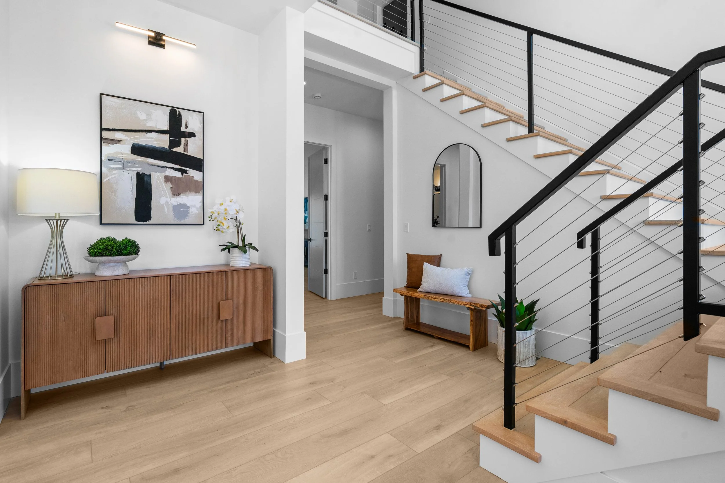 Modern entryway with a wooden console table, abstract artwork, and a staircase with wooden treads and black metal railing.