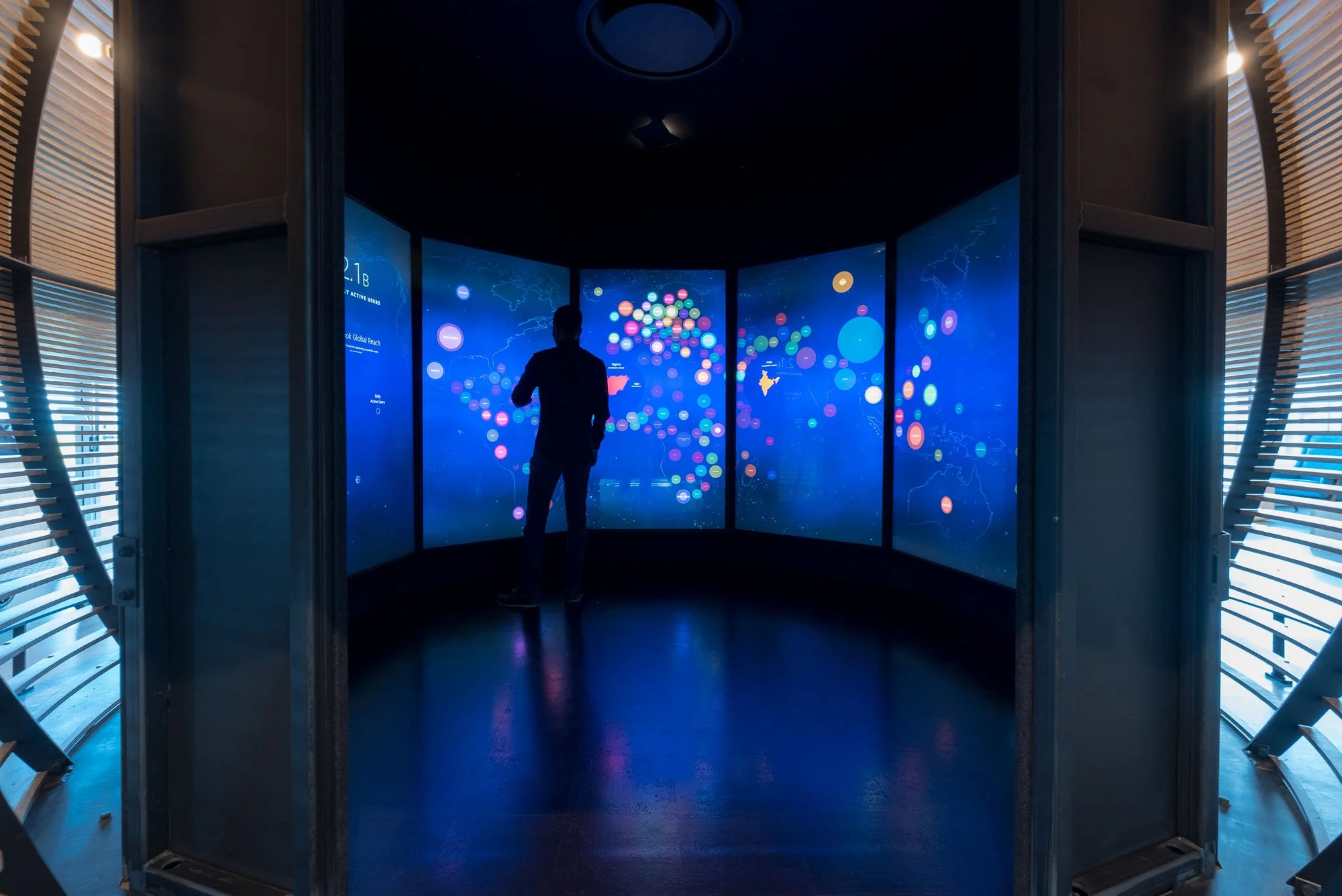 Person standing in front of a large digital display showing various colorful circles and a world map.