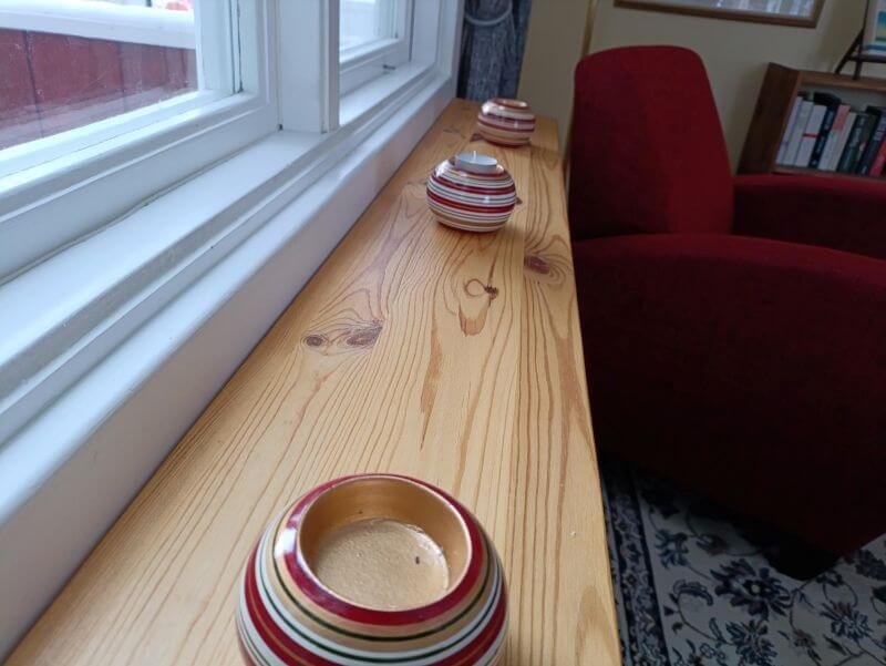 Holzfensterbank mit drei bunten Spirale-Design Vasen neben einem roten Sessel.