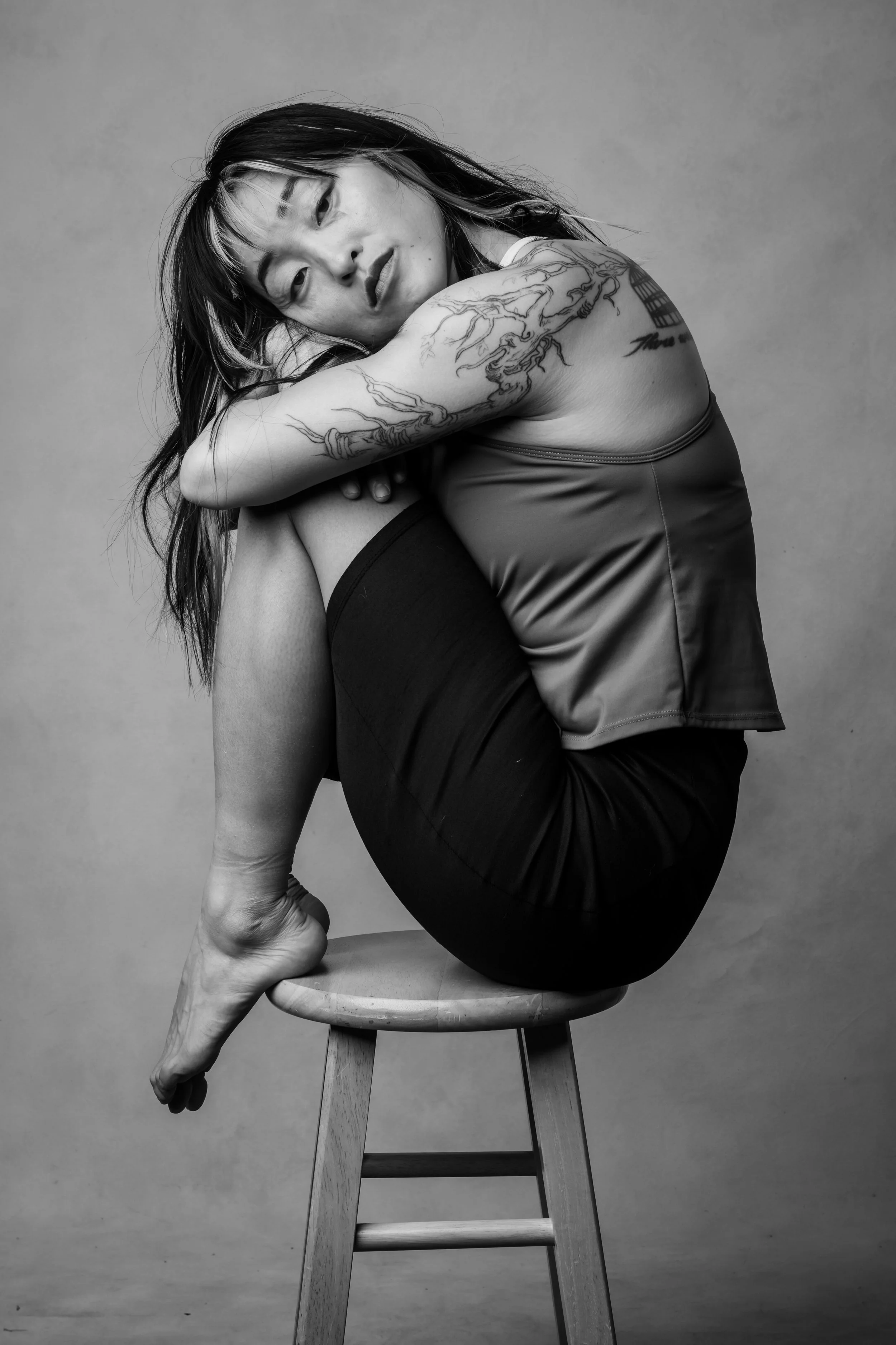 Josie Fouts perched on a stool, a symbol for climbing in precarious places and hugging herself to show self care and softness