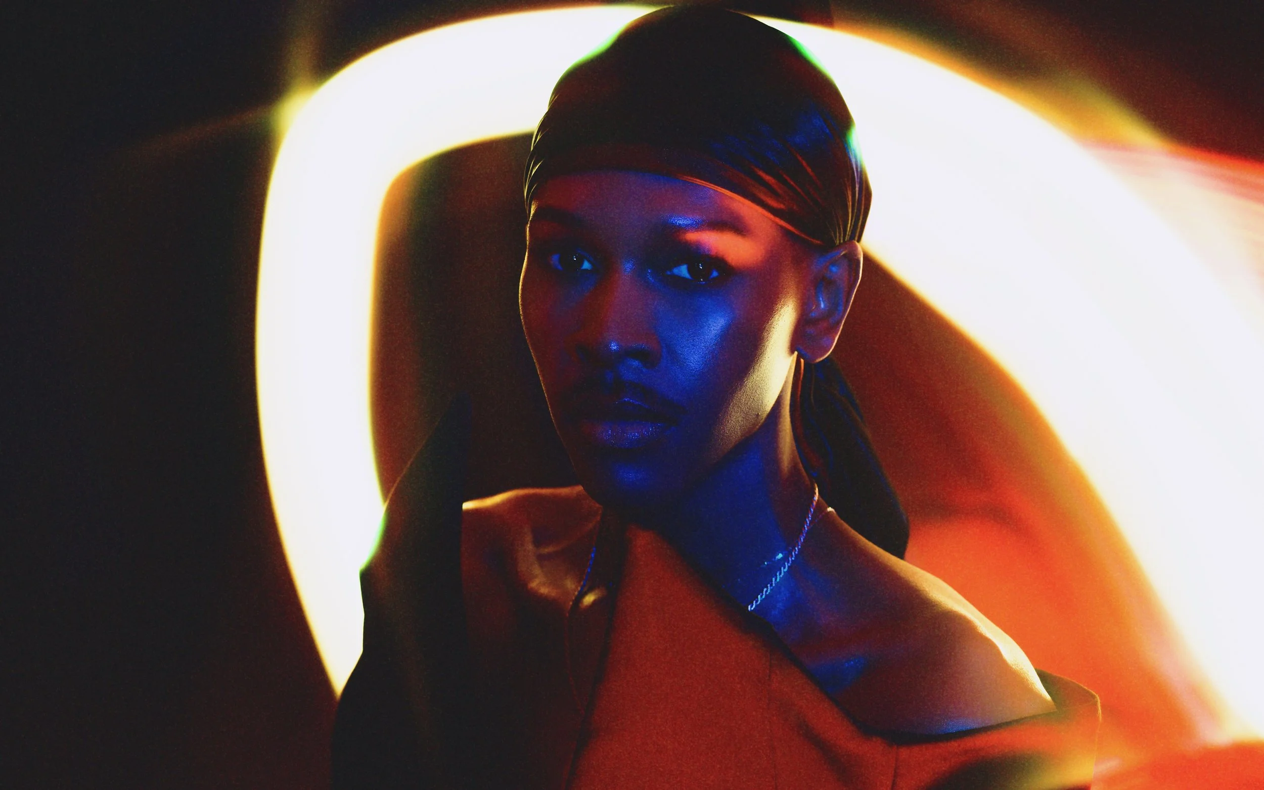 A woman with a scarf in a dark setting illuminated by colored neon lights, creating a vibrant and moody atmosphere.