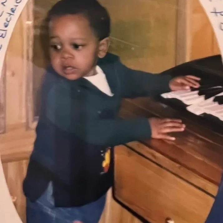 A young boy with dark hair playing a piano in a wooden room.