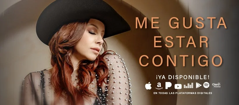 A woman with long wavy red hair wearing a large black hat and a sheer top with pearls, with Spanish text 'Me gusta estar contigo' and logos of music streaming services.