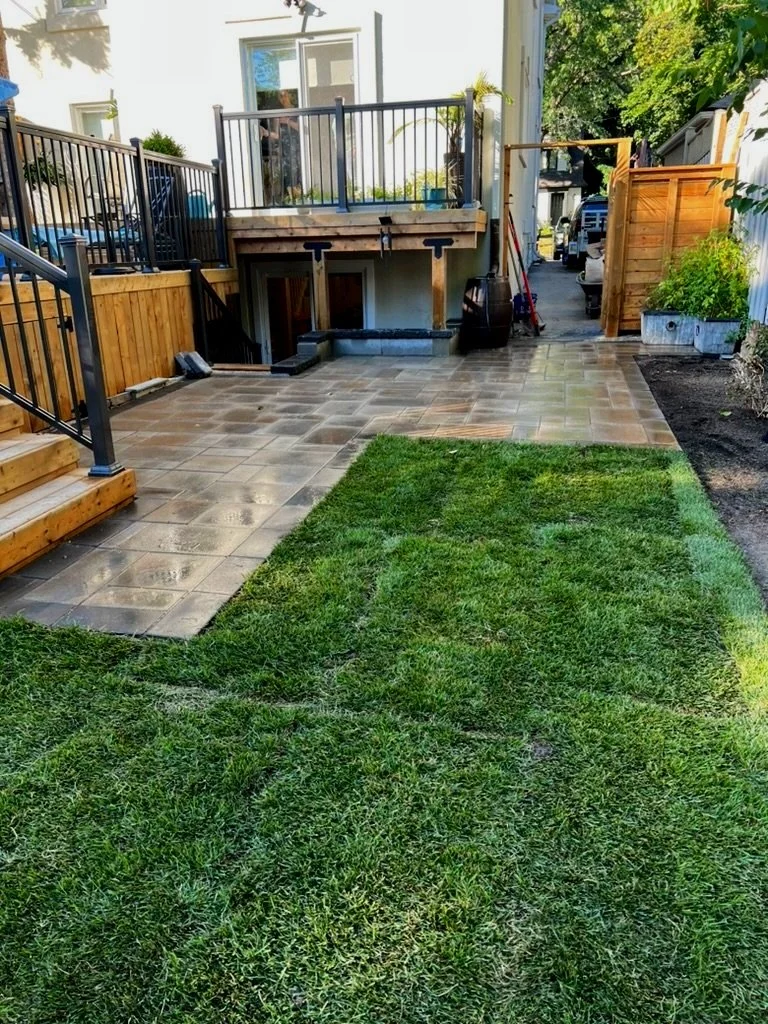 Backyard with newly installed patterned concrete patio, wooden stairs with black metal handrails, and a small lawn area.