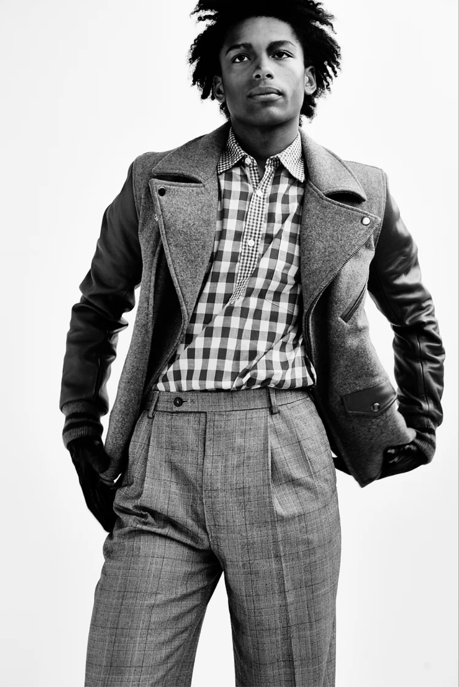 A photo of a male model wearing a striking look of black army, boots, pattern trousers, a leopard print blazer, and a felt hat. the photo is in black-and-white.