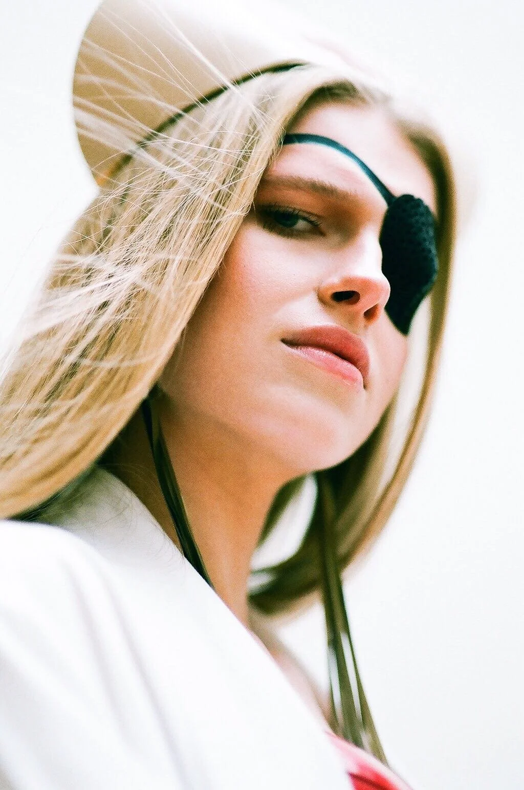 A portrait photo of a white female model with blonde hair. She is dressed as an actress from Kill Bill, wearing a nurse’s outfit with a latex nurse hat and a latex black eyepatch.