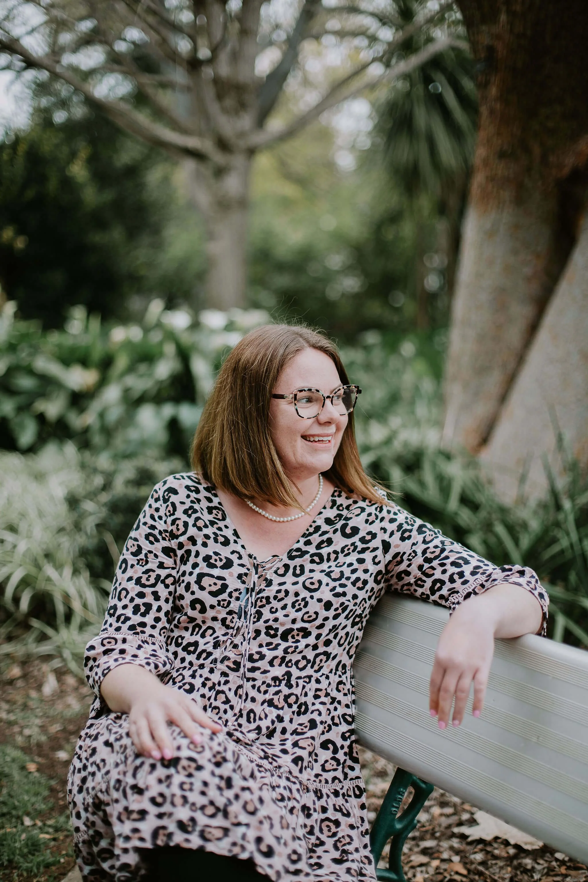 felicity haylock sitting on a park bench smiling looking at the distance