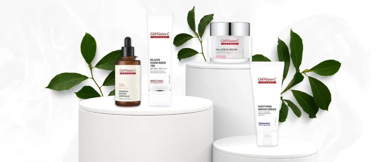 Skincare products from Cell Fusion C on white platforms with green leaves in the background, including sunscreen, creams, and serums.