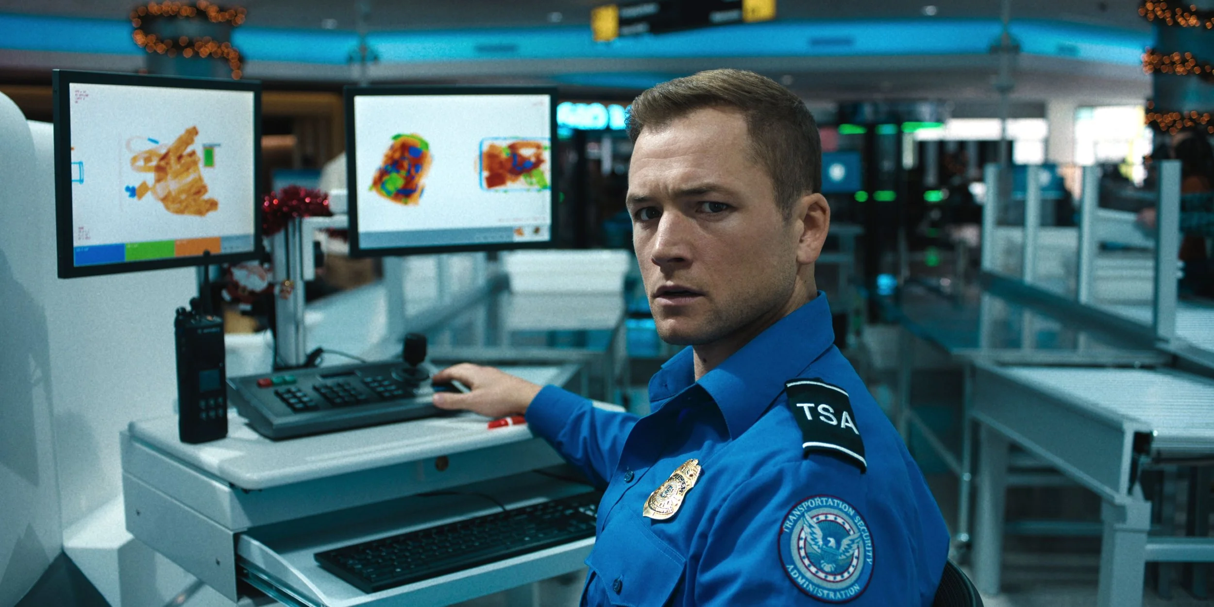 taron-egerton-in-a-tsa-uniform-looking-concerned-with-a-monitor-behind-him-in-carry-on.jpg