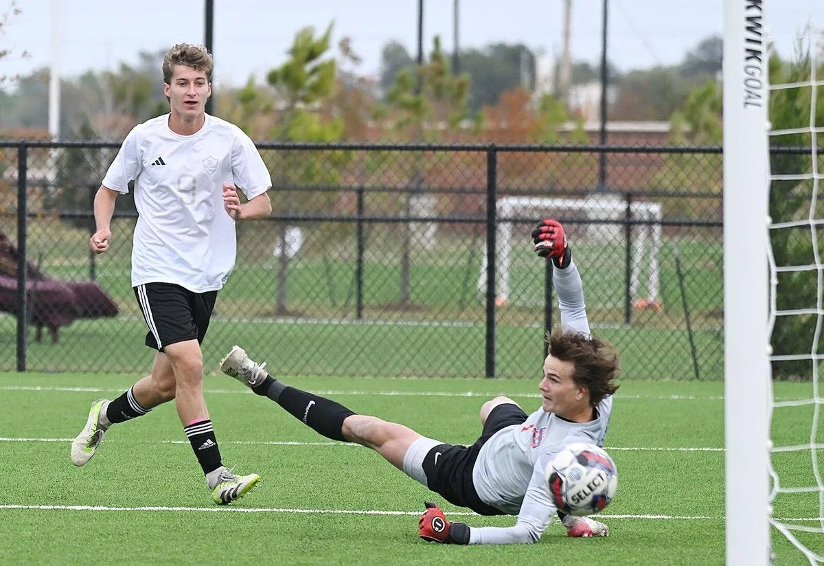Soccer player in white jersey with number 9 running past goalkeeper making a save on a field.