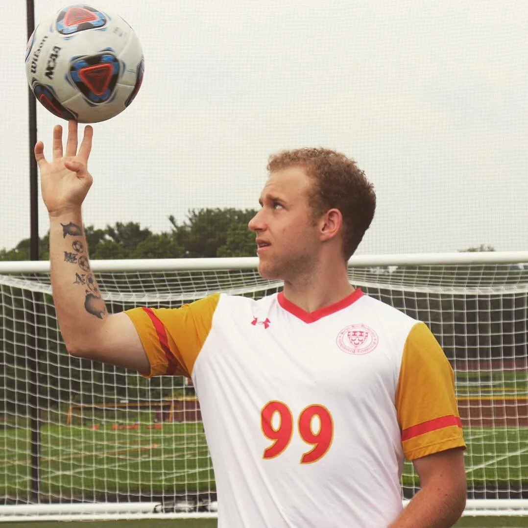 Soccer player in a white and yellow jersey with number 99, spinning a soccer ball on his finger in front of a goal net.