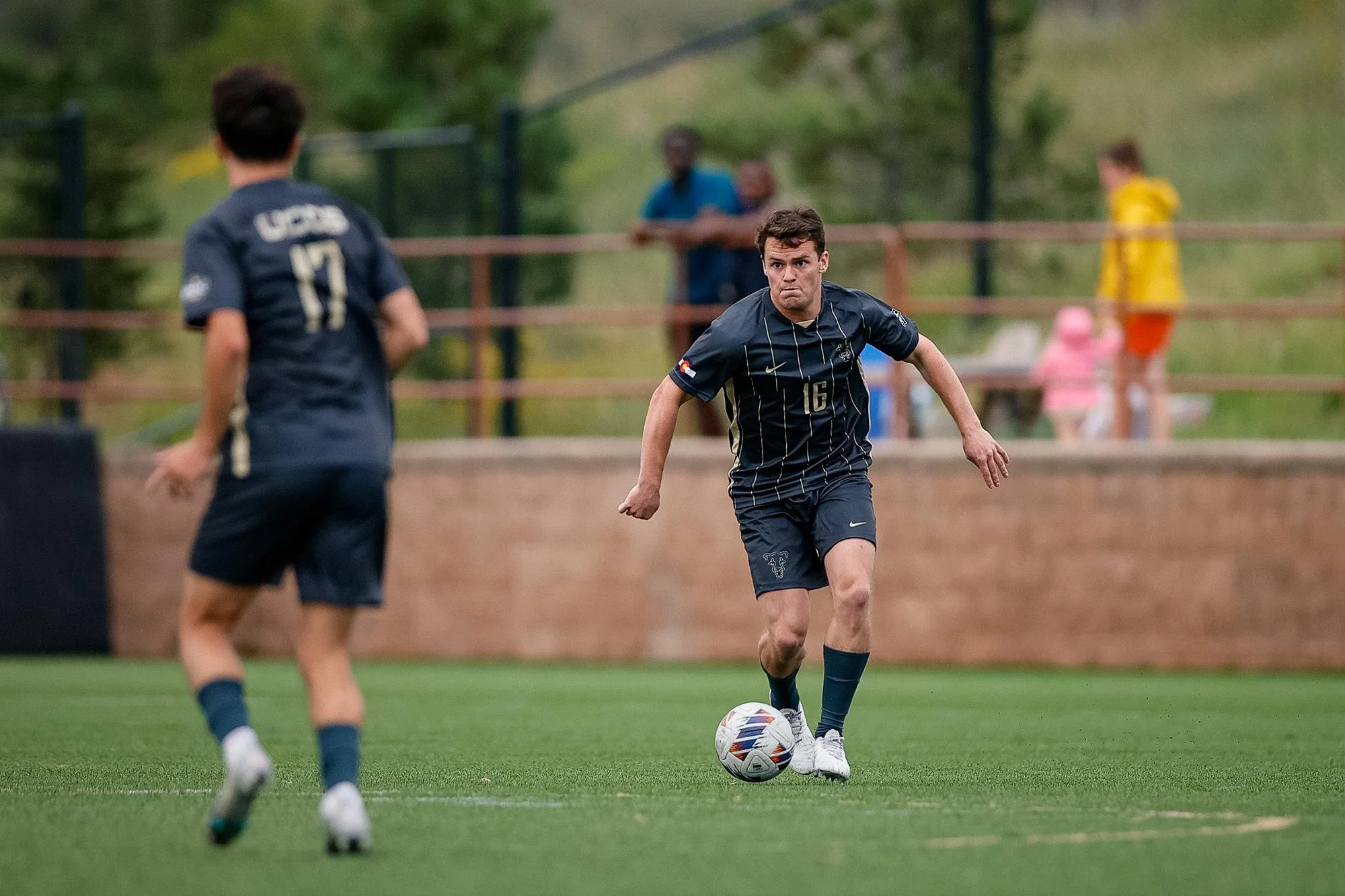 Soccer player in dark uniform dribbling a ball on a field.