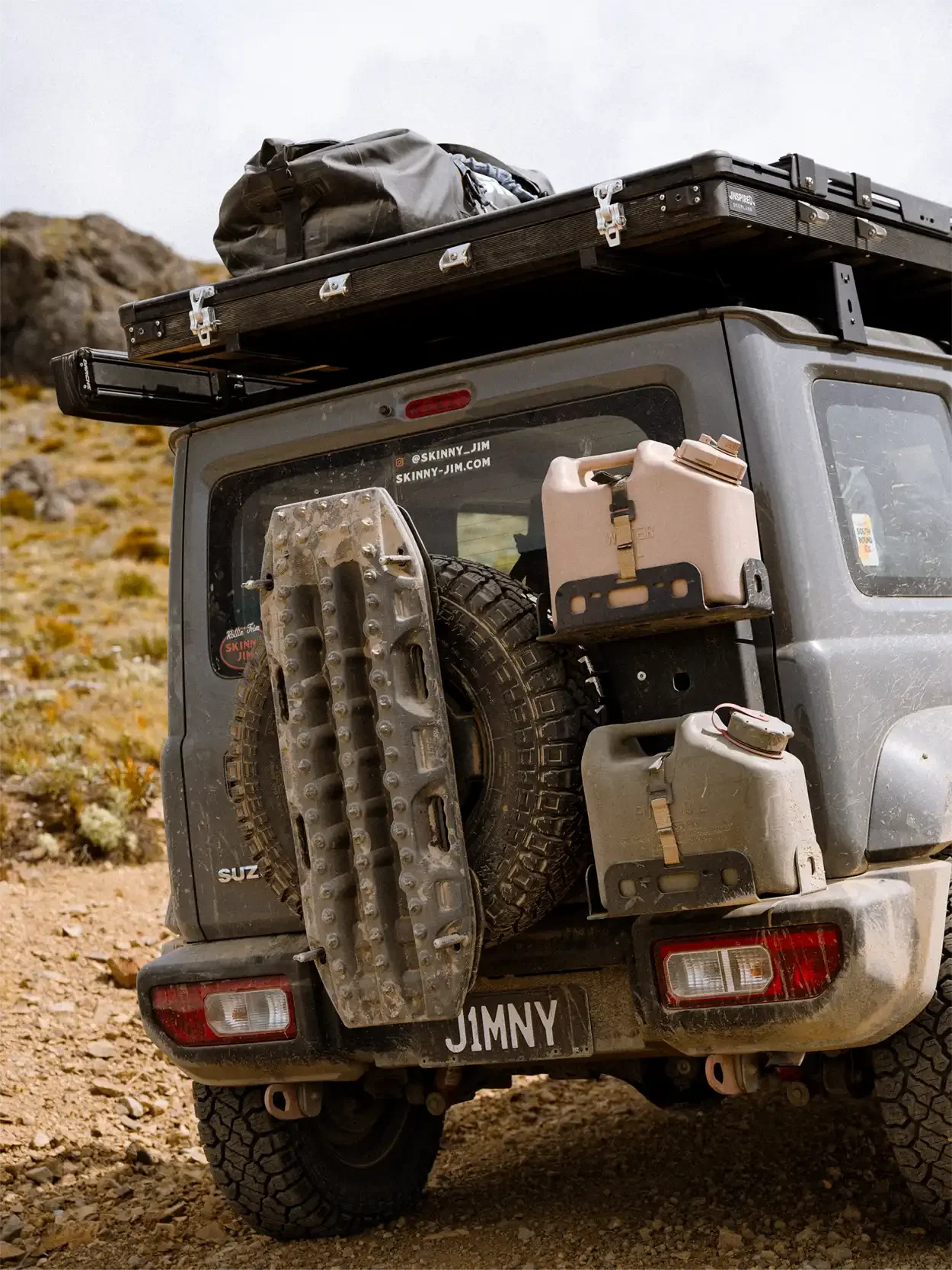 Jerry can and recovery track attached to the rear of a grey Suzuki Jimny on high country dirt road