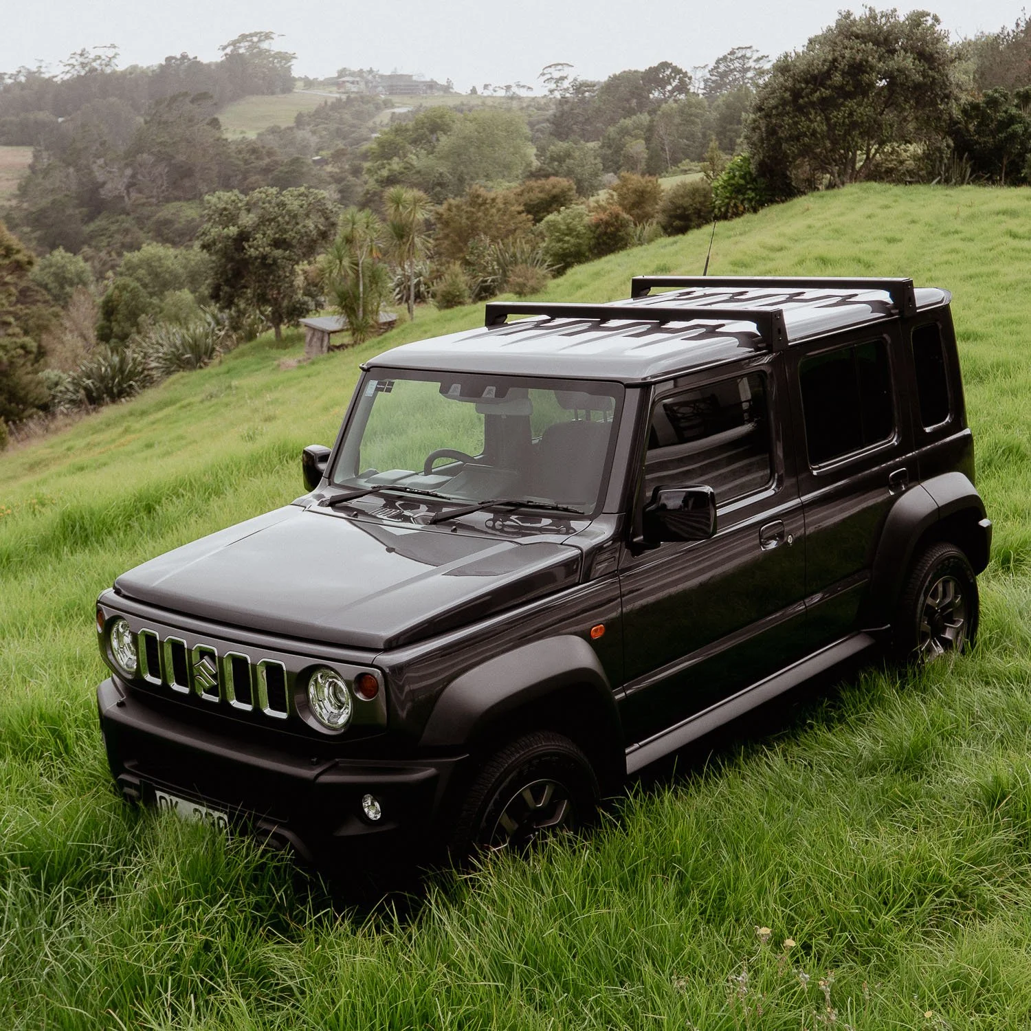 Suzuki Jimny 5-door with roof rack, parked in long grass