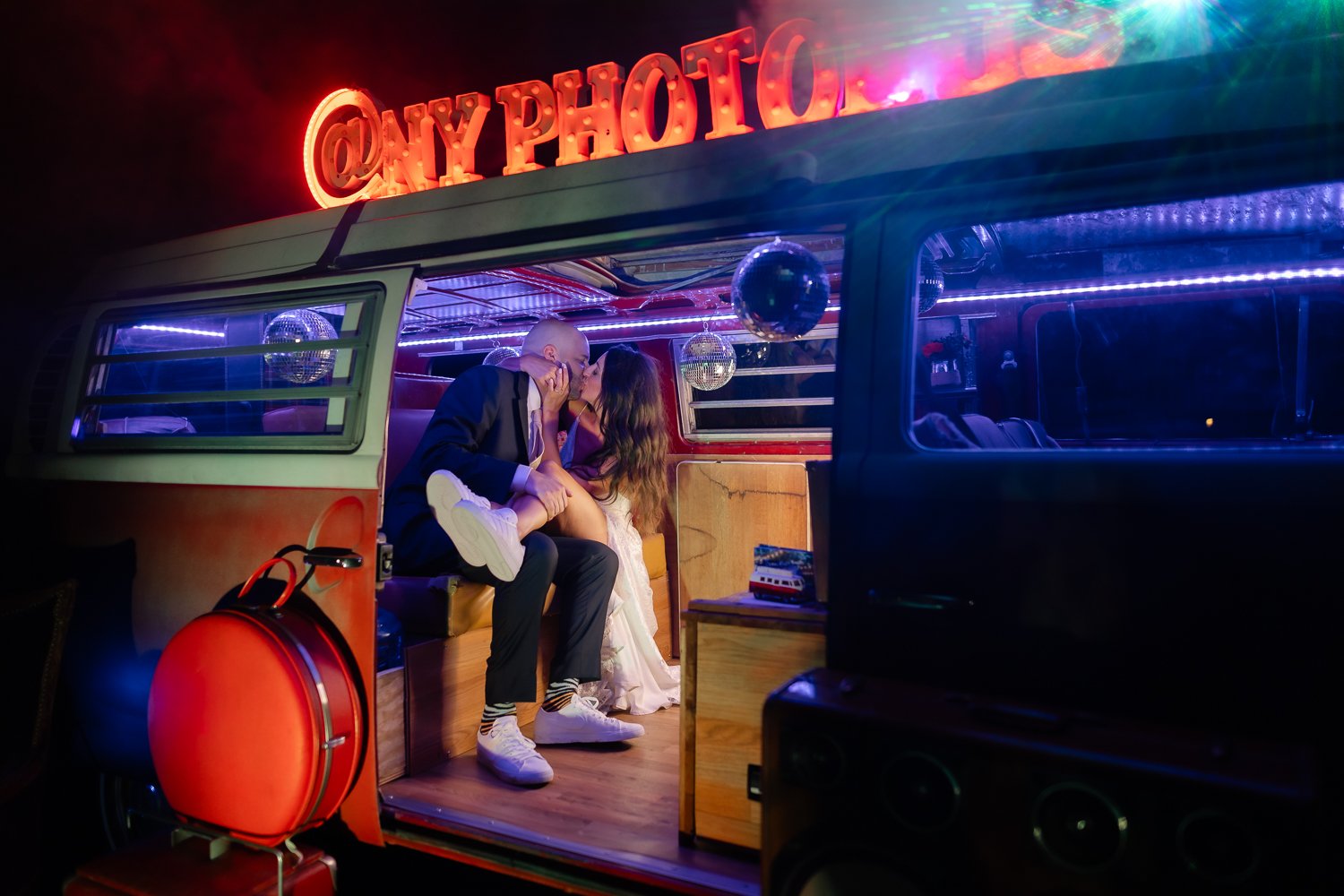 Couple kisses inside NY Photobus lit up at night.