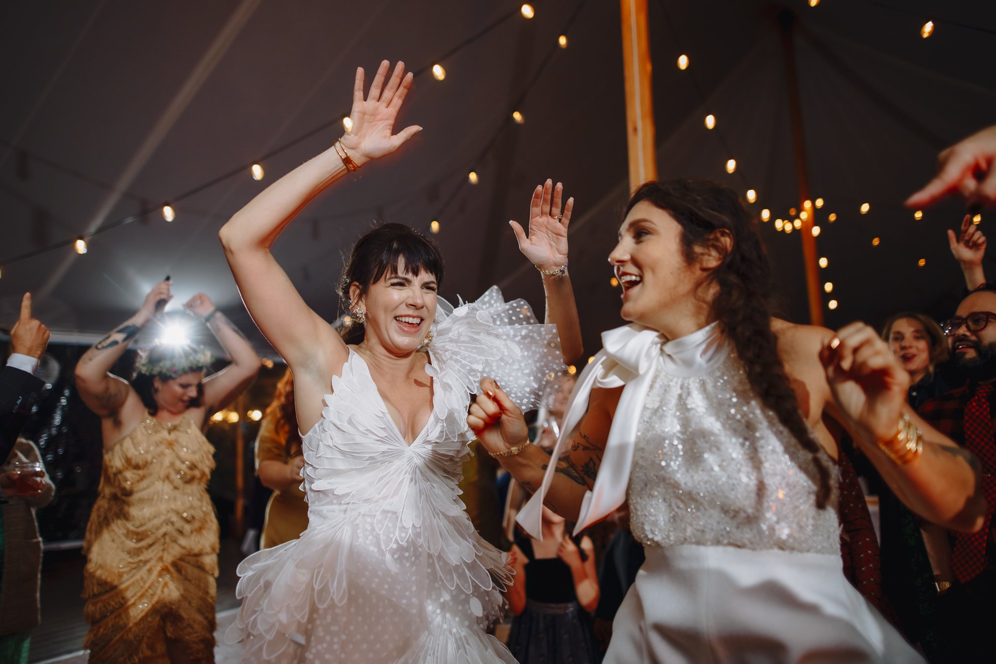 Brides dancing joyfully during their wedding reeception with string lights in a tent