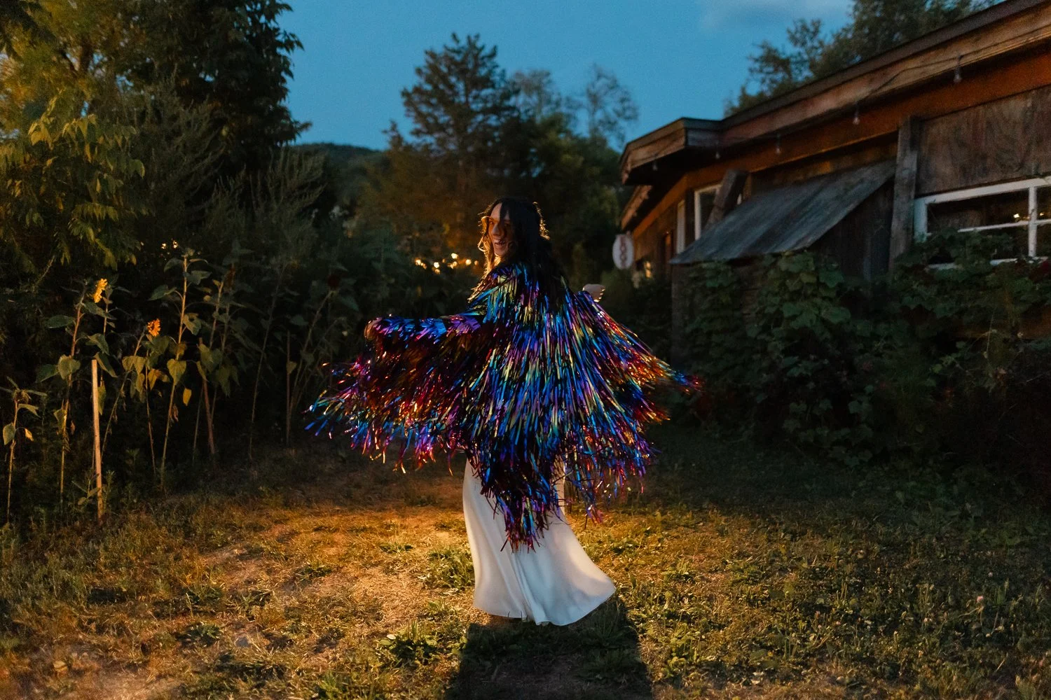 Bride shimmies in glitter streamer coat portraits outside her party.