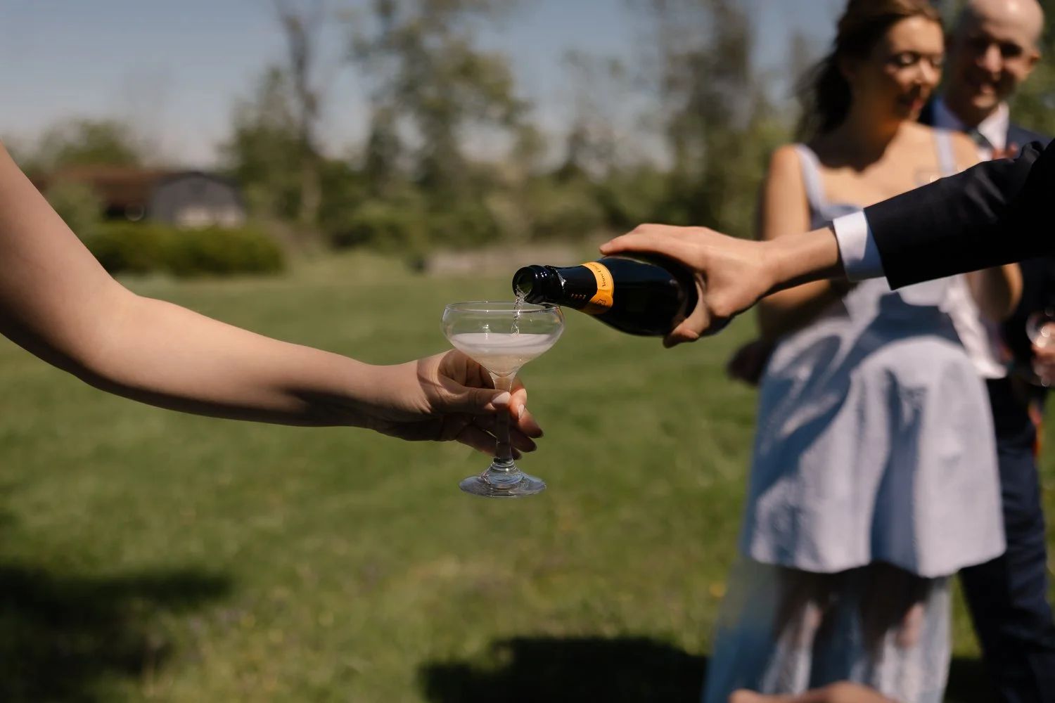 close up of hands pouring champagne and holding glass.