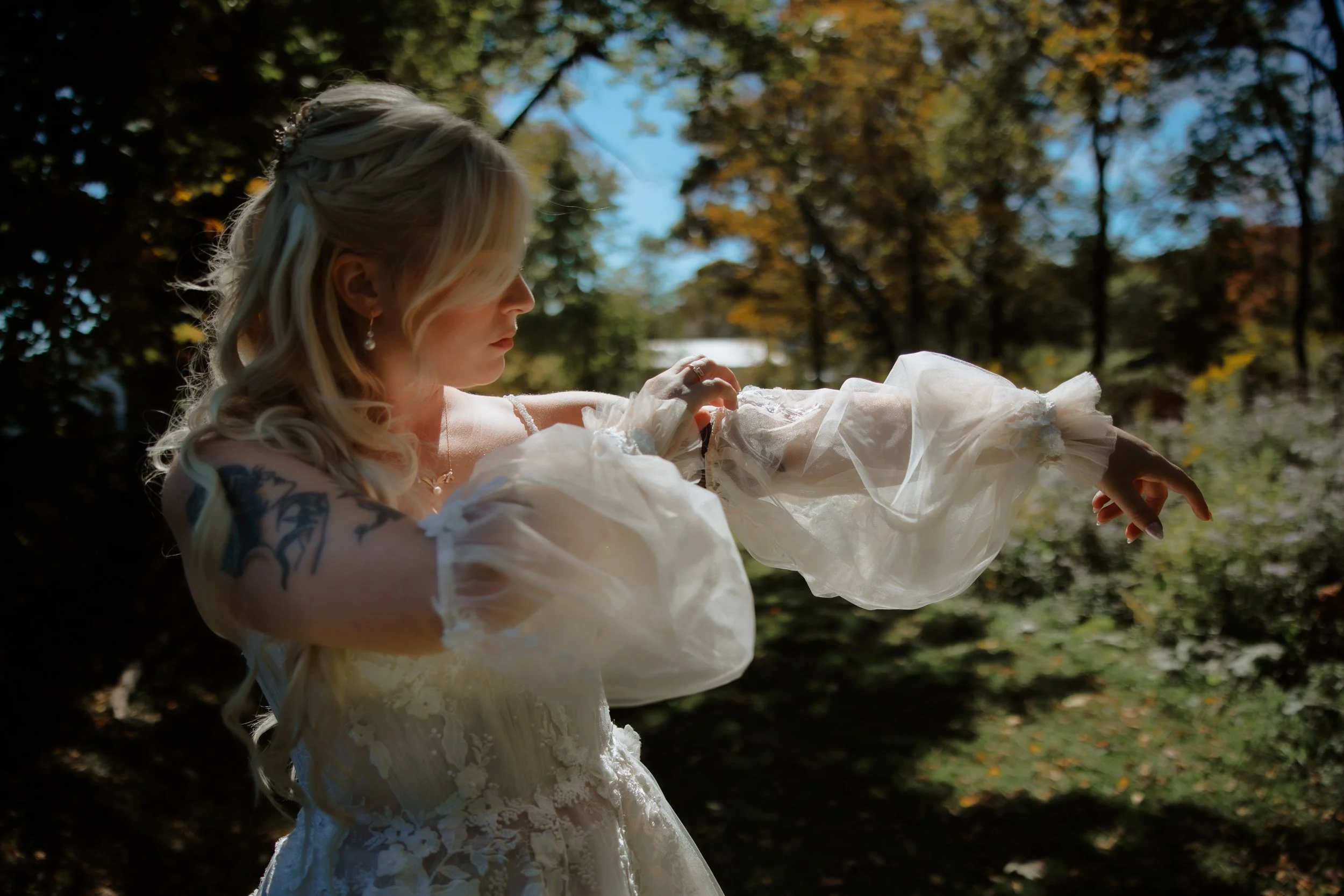 Bride adjusting the sleeve of her lace gown in a wooded setting near Kingston.