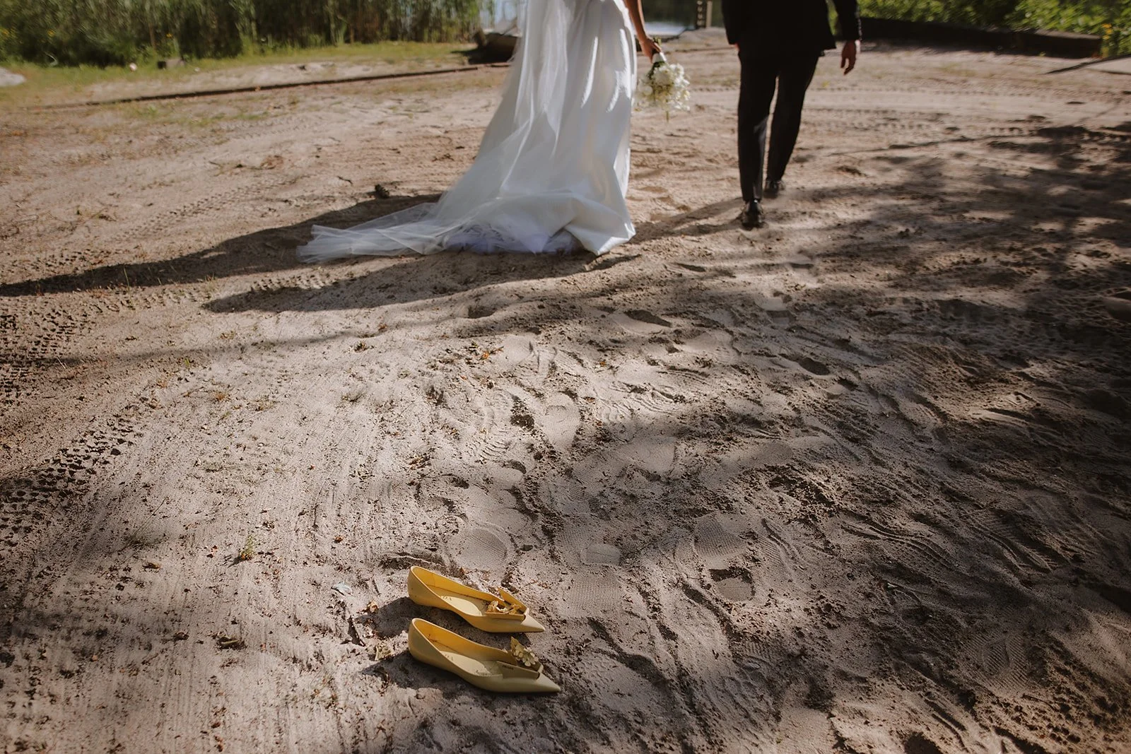 Bride's yellow wedding shoes left in the sand as the couple walks along the shoreline.