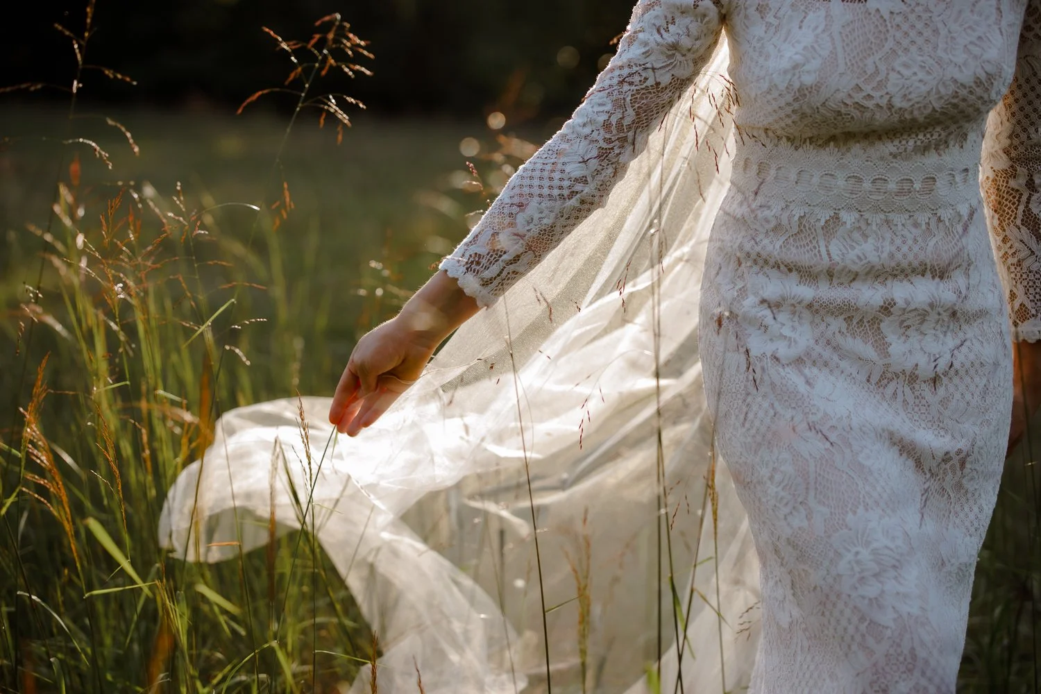 Detail of a lace wedding gown brushing through tall grass near New Paltz.