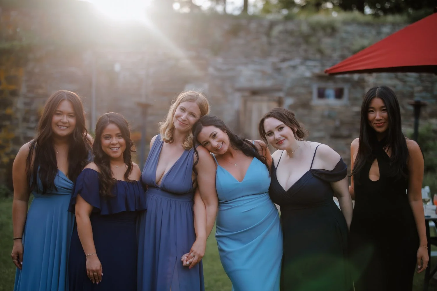 Bridesmaids in shades of blue posing together outside a stone venue.