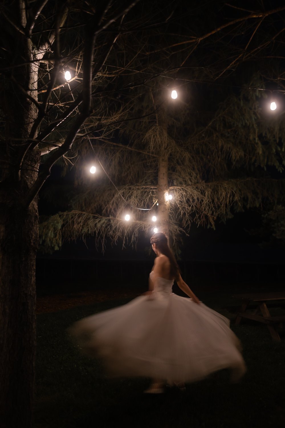 bride dances under string lights at night in blurry romantic portrait.