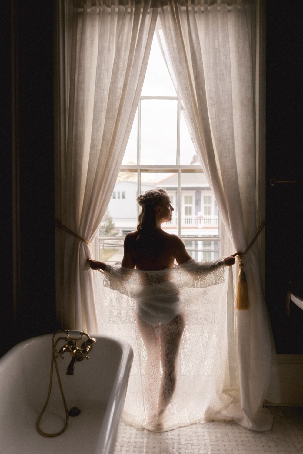 Bride stand at floor length window in silhouette naked with sheer robe.
