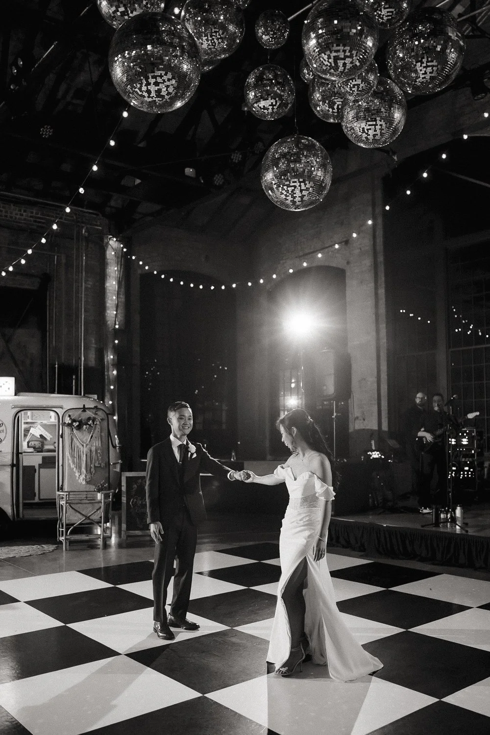 Bride and groom sharing their first dance under disco balls on a checkered dance floor.