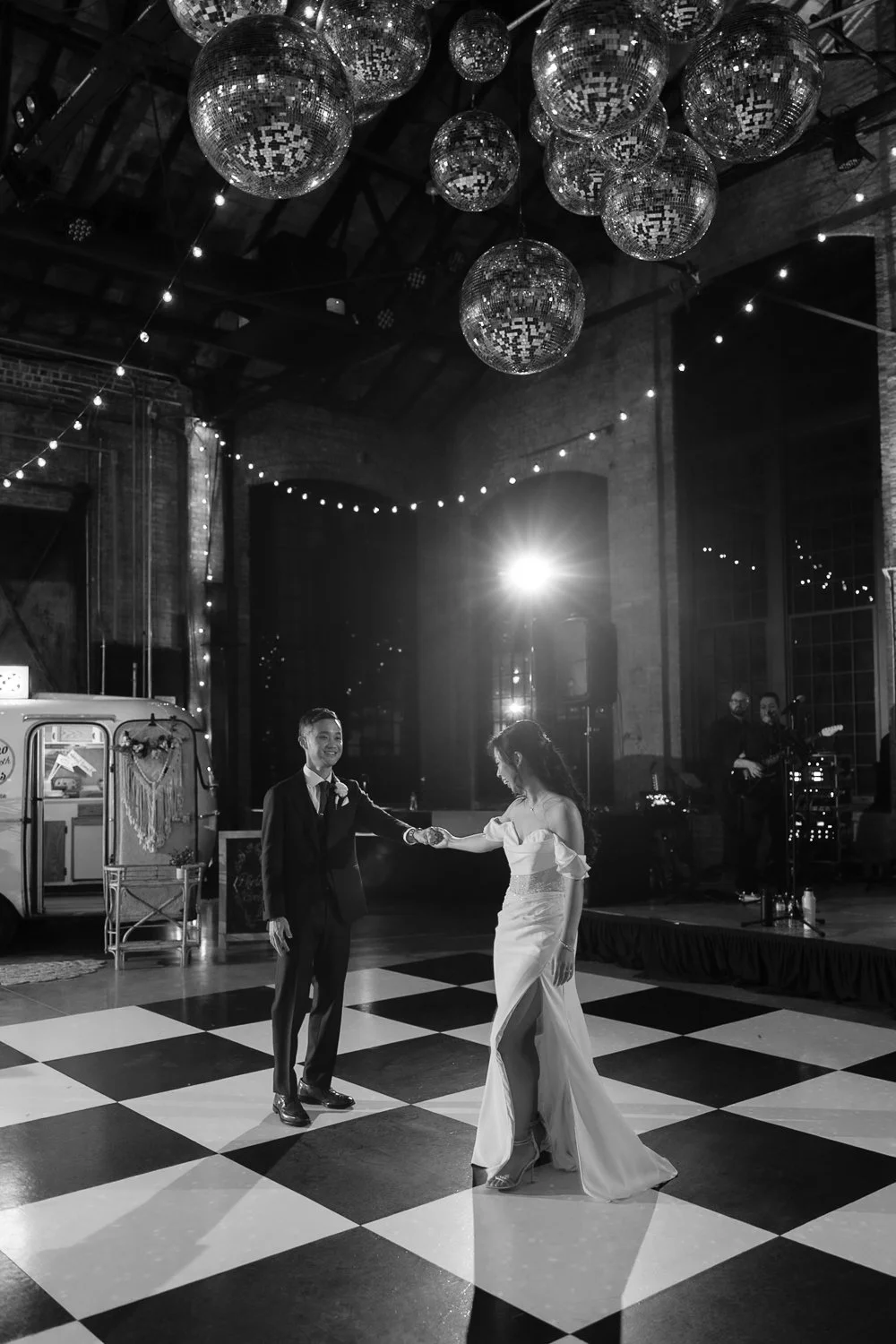 Couple shares their first dance under several disco balls on checkered dance floor.