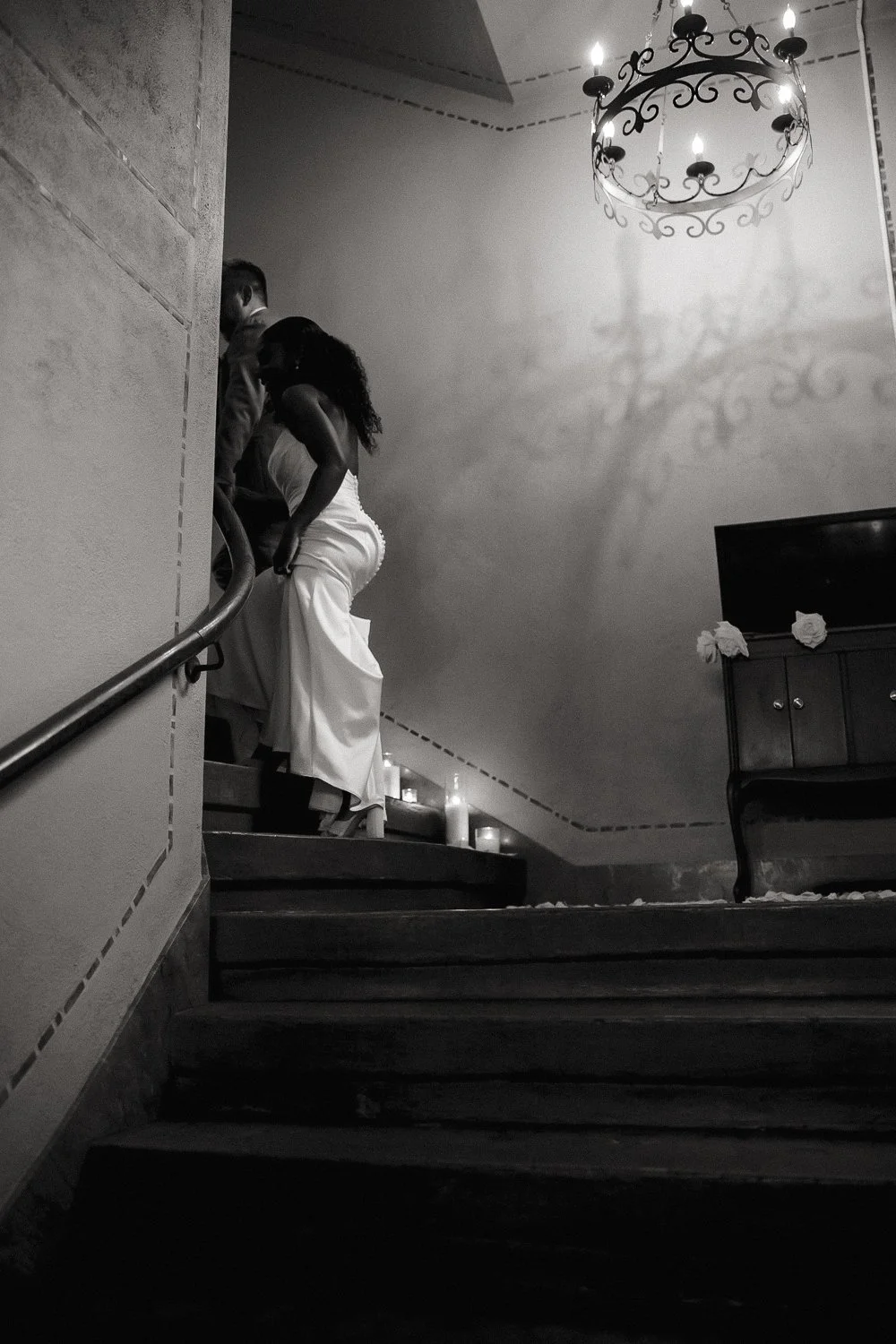 Bride and groom descending a candlelit staircase in black and white.