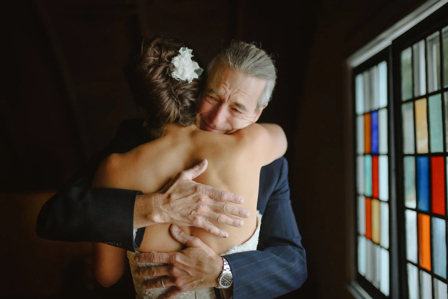 Father embracing his daughter in an emotional moment beside a stained glass window before the ceremony.