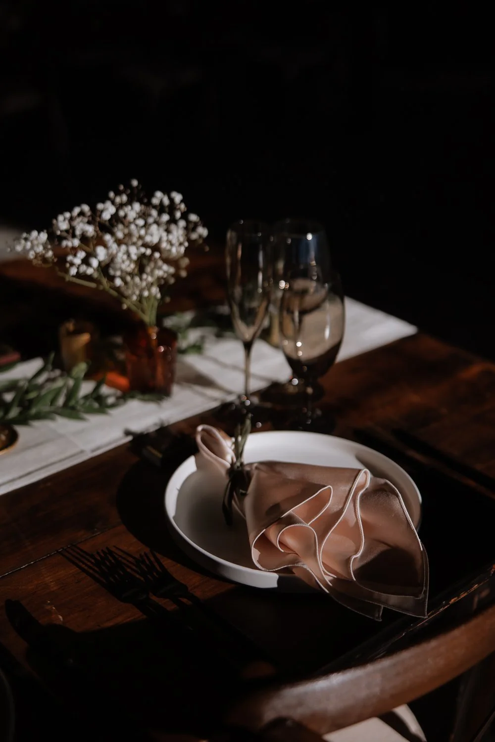 Sunlit reception table setting with soft florals and folded linen napkins.