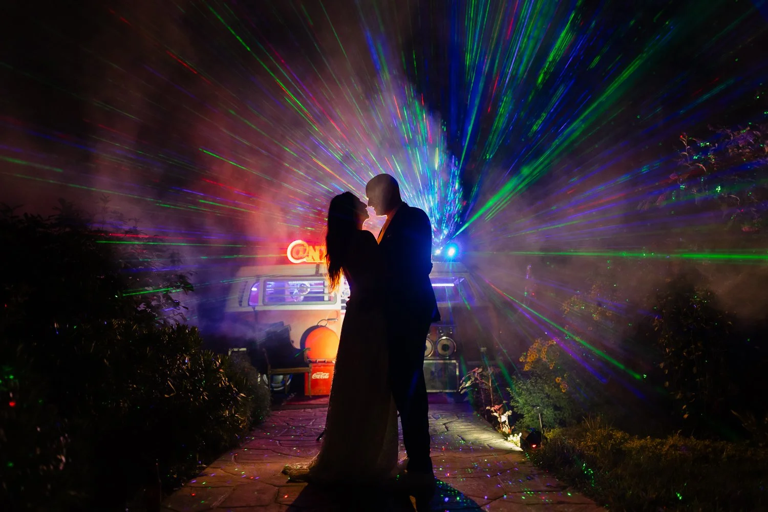 Couple is silhouetted against laser lights from VW bus photobooth.