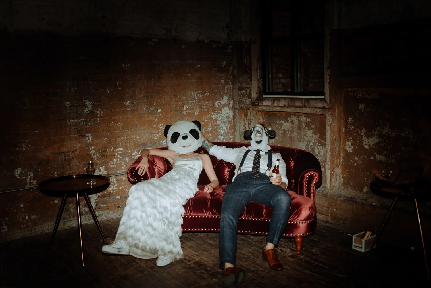 Couple relaxes on a red couch with furry animal heads on.