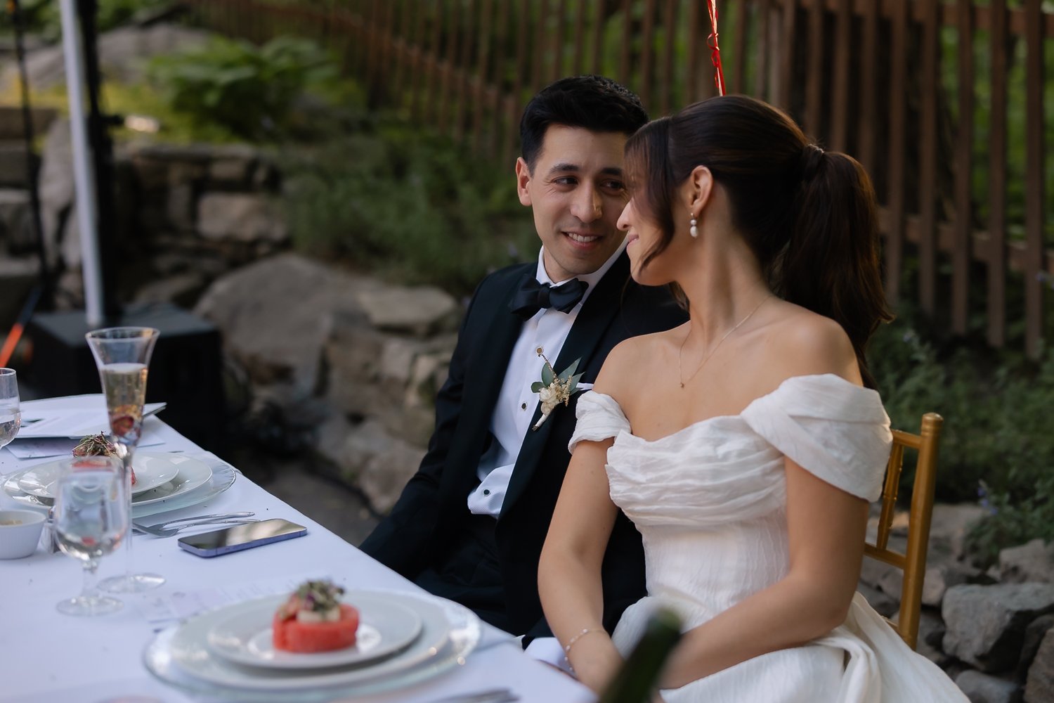 Groom looks lovingly at bride while sitting listening to wedding speeches.