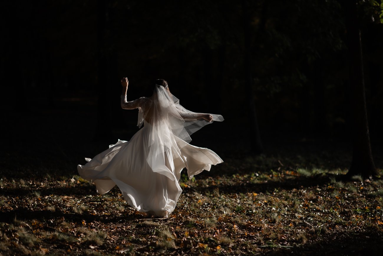Bright sunlight captures the texture of a brides white dress as she twirls in the forest.