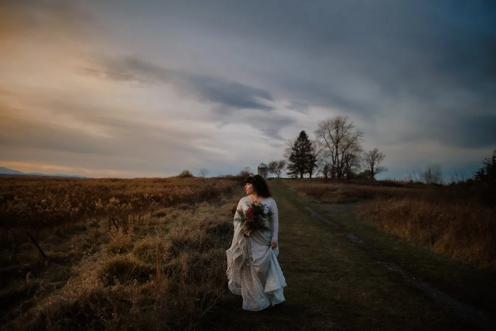 Bride in a flowing gown walking alone through a golden field near Rhinebeck at dusk.
