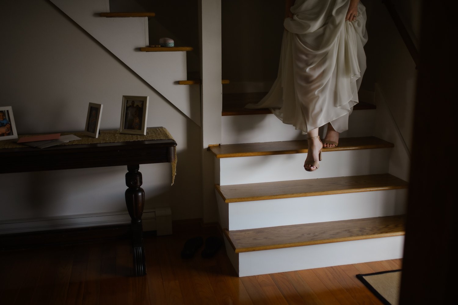 Bride lifting her gown as she steps down a wooden staircase in a quiet home before the ceremony.