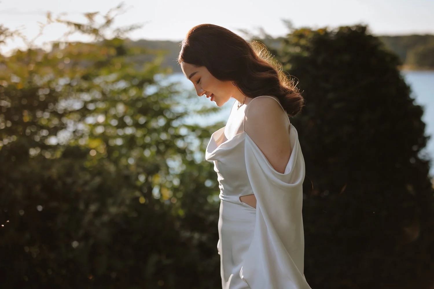 Bride in a flowing white gown looking out over the water near Cold Spring at golden hour.