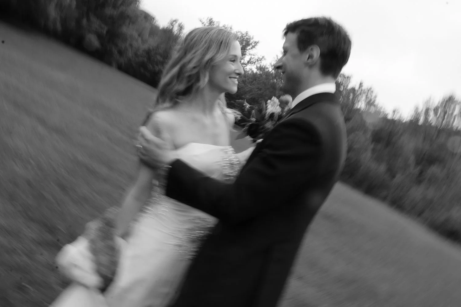 Blurry photo of couple smiling at each other in field after their wedding vows.