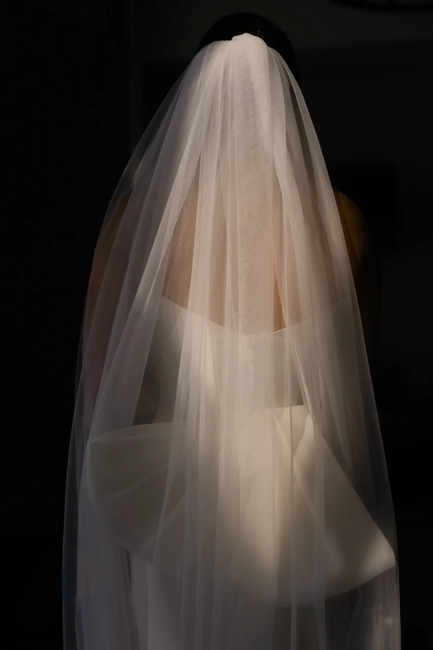 A mannequin wearing a wedding veil and strapless wedding dress, with a dark background.