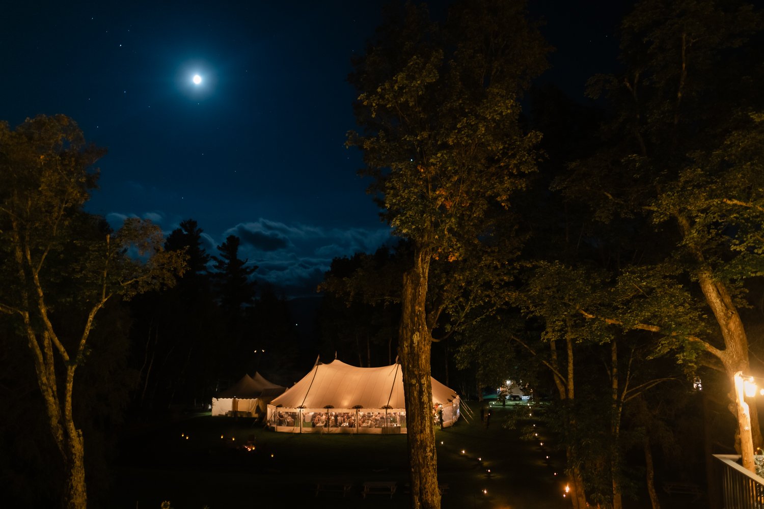 Sailcloth tent is lit up under blue night sky with stars.
