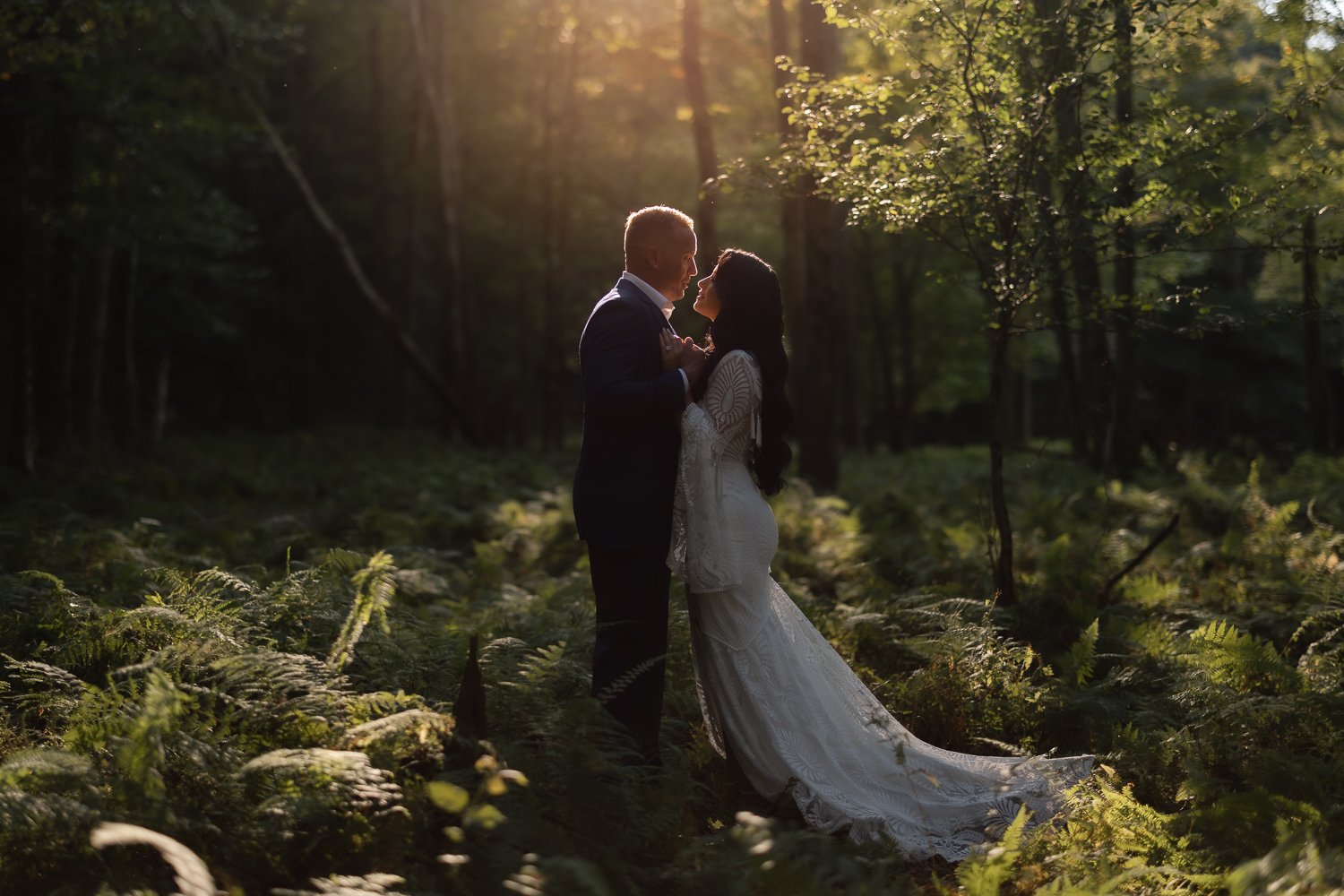 Couple shares intimate moment standing in fern forest after wedding.