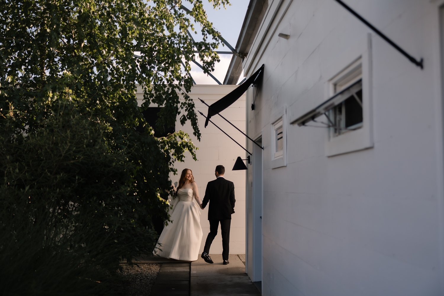 Couple takes editorial portraits outside white motel room alley with golden light.